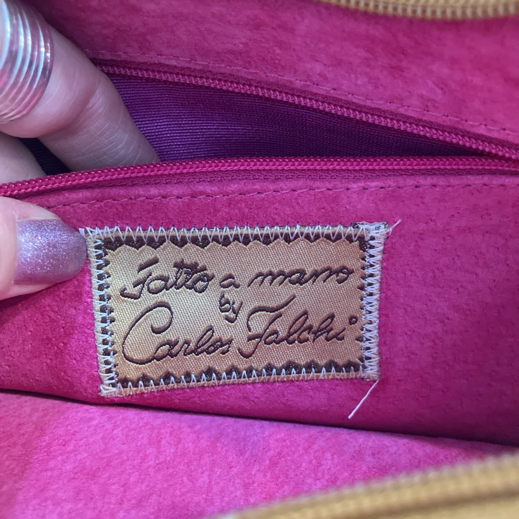 Close-up of a pink fabric pouch or bag interior with a zipper and a sewn label reading 'Fatto a mano by Carlos Falchi'. A hand with glittery purple nail polish and a silver ring is holding the edge of the pouch.