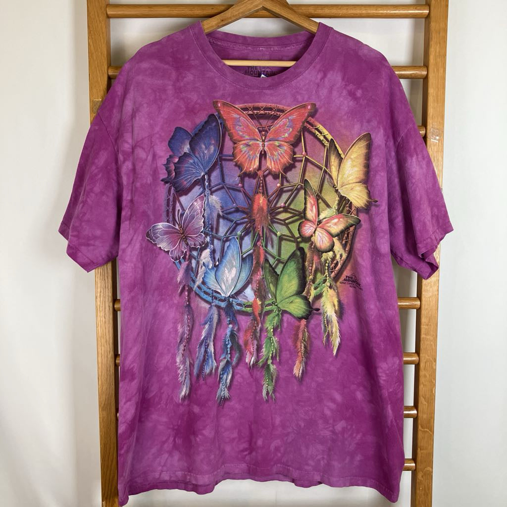 A purple tie-dye short-sleeve t-shirt hanging on a wooden hanger, featuring a large colorful graphic of a dreamcatcher with various butterflies in shades of blue, pink, orange, and green.
