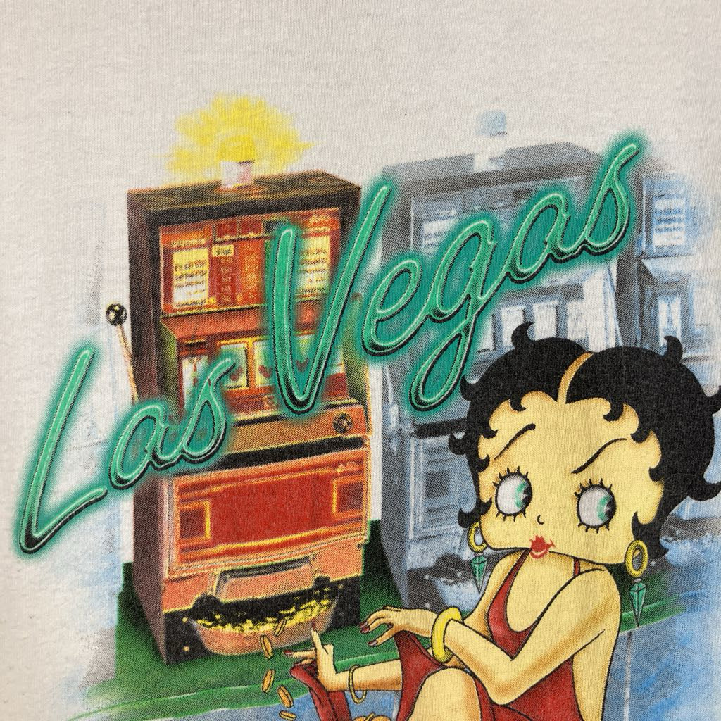 A vintage-style illustrated scene with the words 'Las Vegas' in large teal script over a slot machine and a cartoon woman resembling Betty Boop, seated in a city setting.