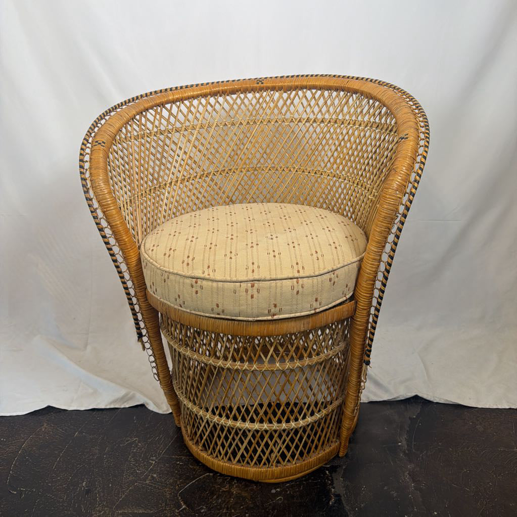 A vintage-style woven rattan barrel chair with a curved backrest and a round upholstered seat cushion, shown against a white fabric backdrop.