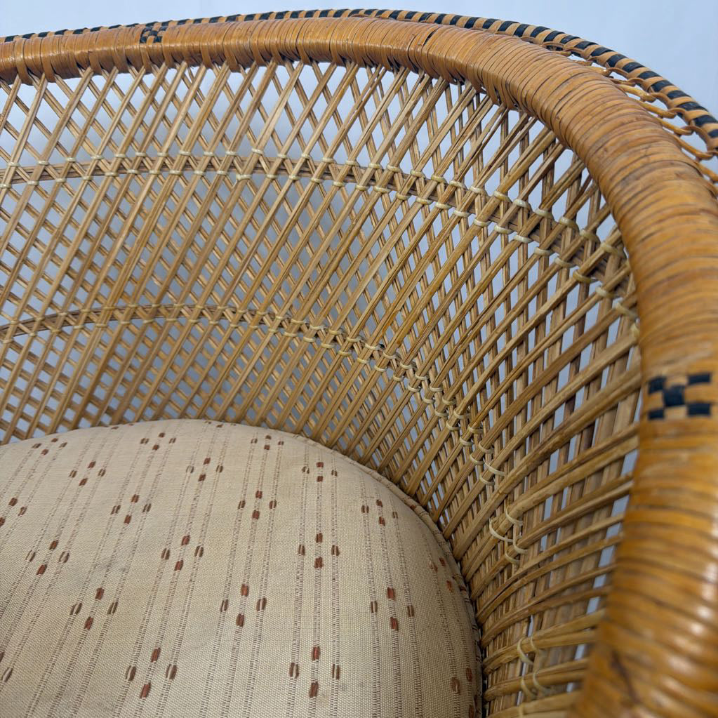 Close-up of a woven rattan chair with a curved armrest and a round upholstered seat cushion in beige fabric with small brown dotted patterns.