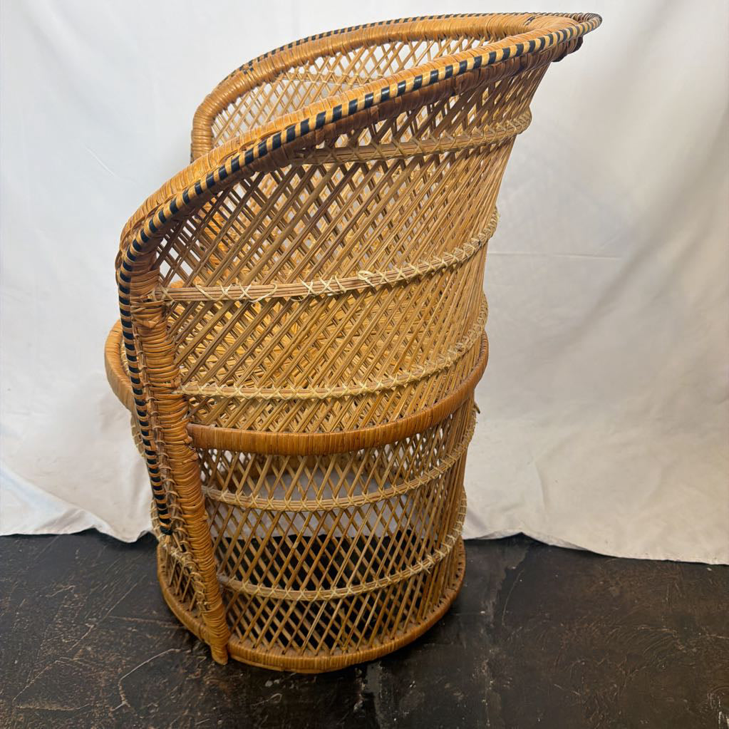 A vintage woven rattan chair with a curved back and seat, shown from a side angle against a white fabric backdrop.