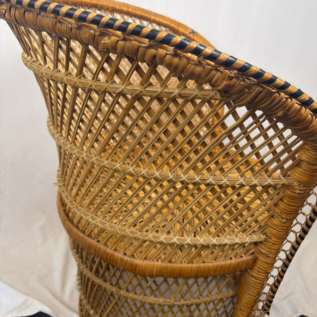 Close-up of a woven rattan chair back, showing natural tan wicker with dark blue painted accents along the top rim and seat bands, set against a light fabric backdrop.