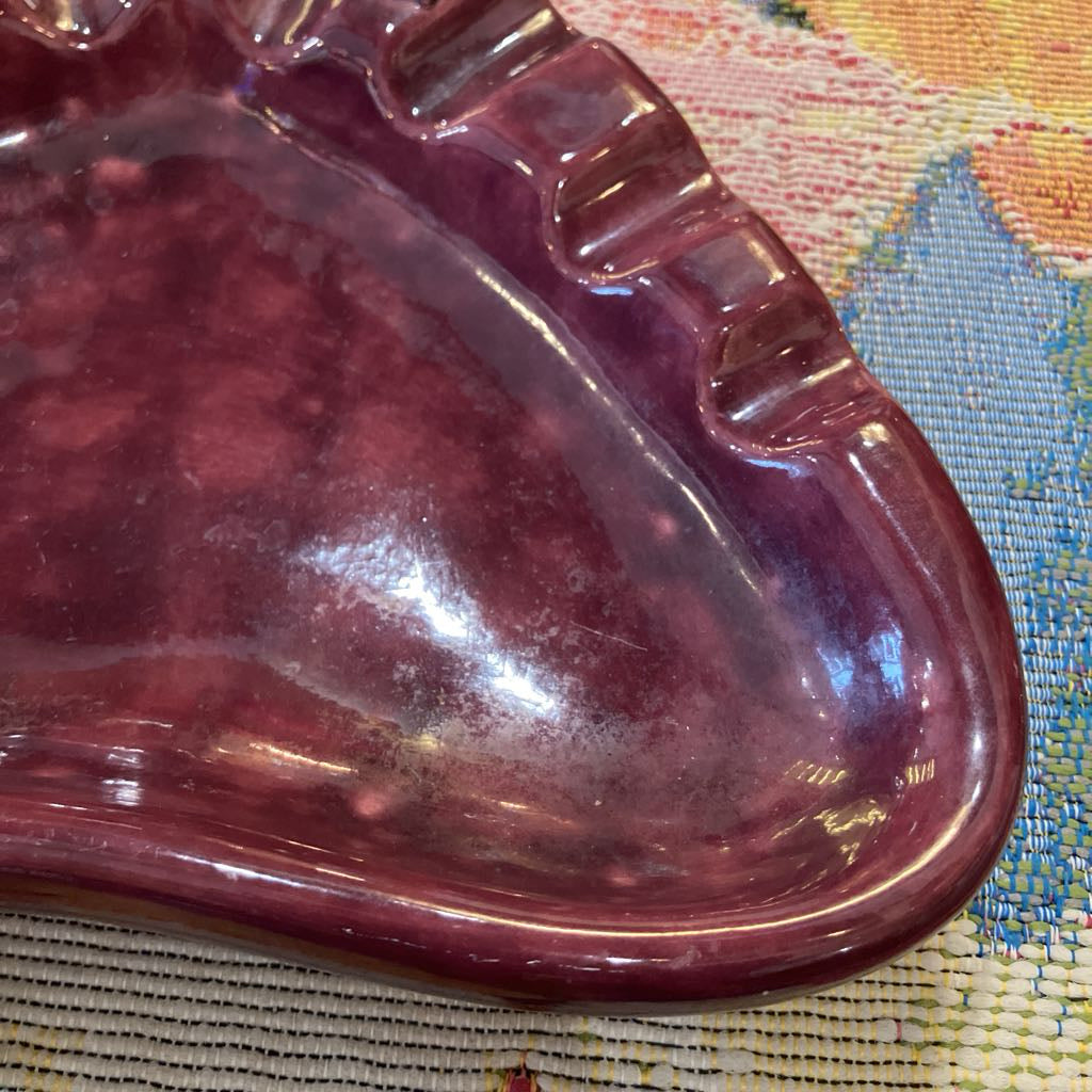 A close-up of a glossy, marbled deep purple glass dish or tray resting on a textured, multicolored woven fabric surface.