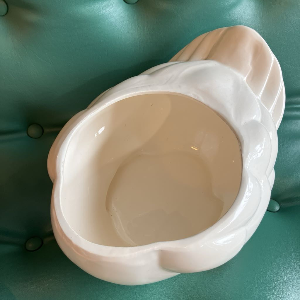 A glossy white ceramic bowl with a sculptural, organic shape, photographed from a top-down angle on a teal tufted leather surface.