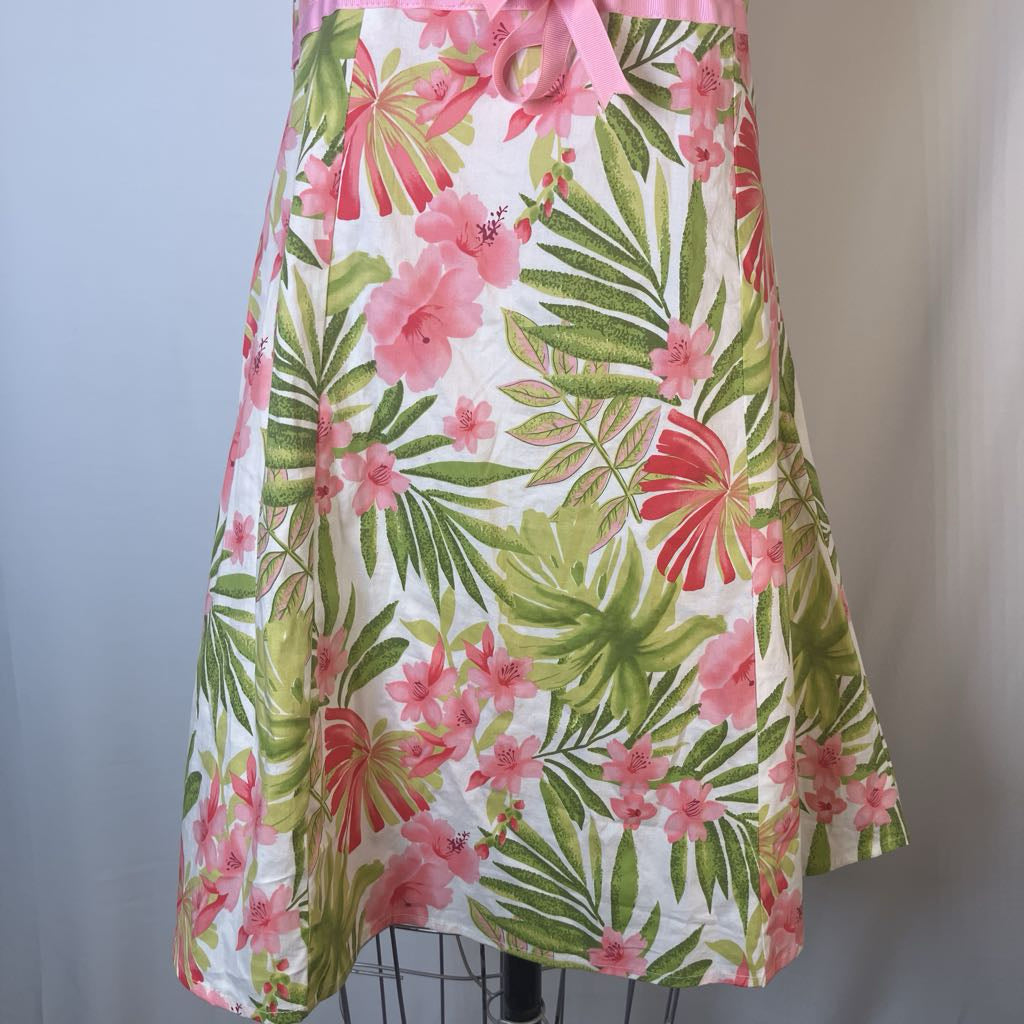 A tropical floral print skirt with pink hibiscus flowers and green palm leaves on a white background, displayed on a dress form with a pink waist tie.