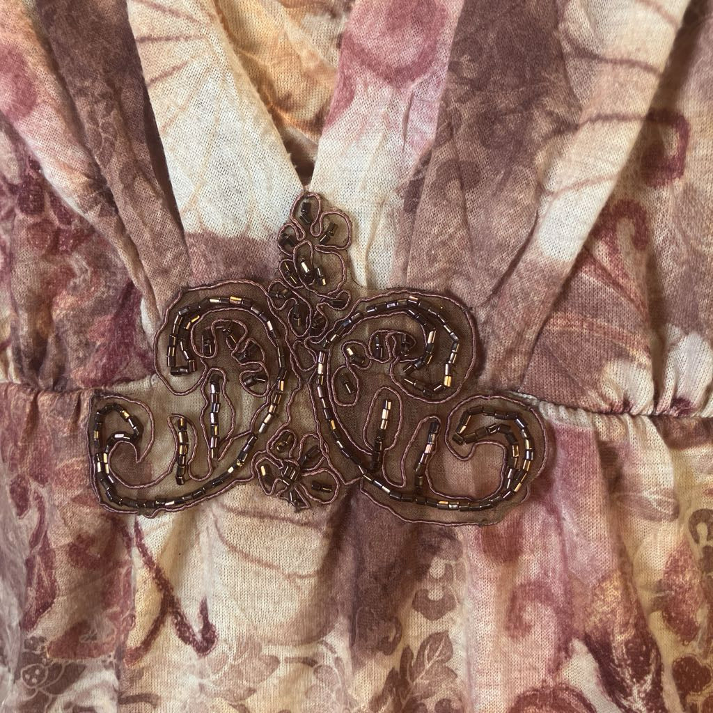 A close-up of a vintage-style dress or garment featuring a brown embroidered scrollwork applique with sequins over a beige and mauve floral patterned fabric.