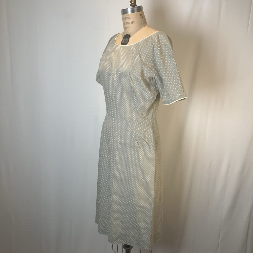 A short-sleeve knee-length dress with a small repeating geometric pattern, displayed on a vintage dress form mannequin against a white fabric backdrop.