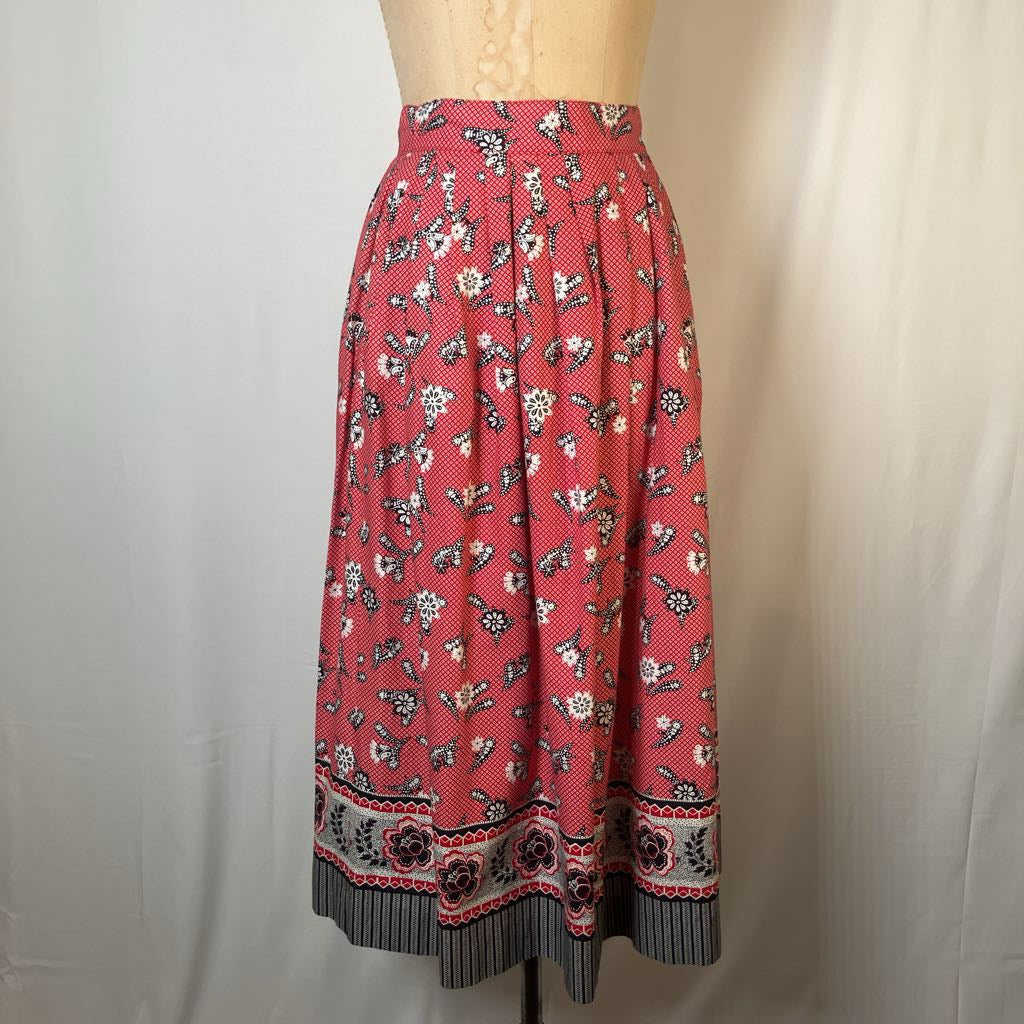 A red midi skirt with a white and black floral print and a decorative border at the hem, displayed on a beige dress form against a light gray fabric backdrop.