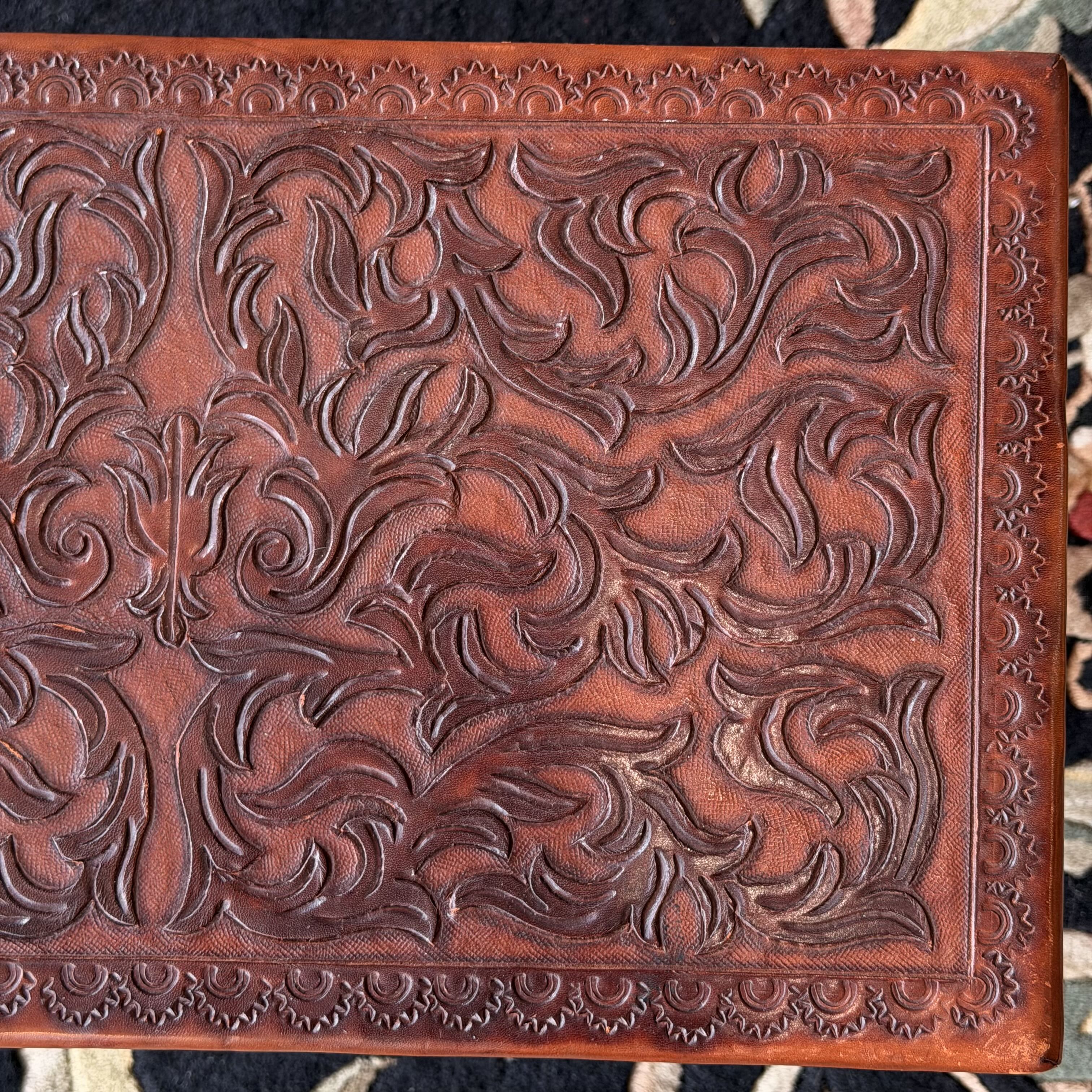 A close-up of a brown leather item featuring an embossed floral scroll pattern and a decorative border.