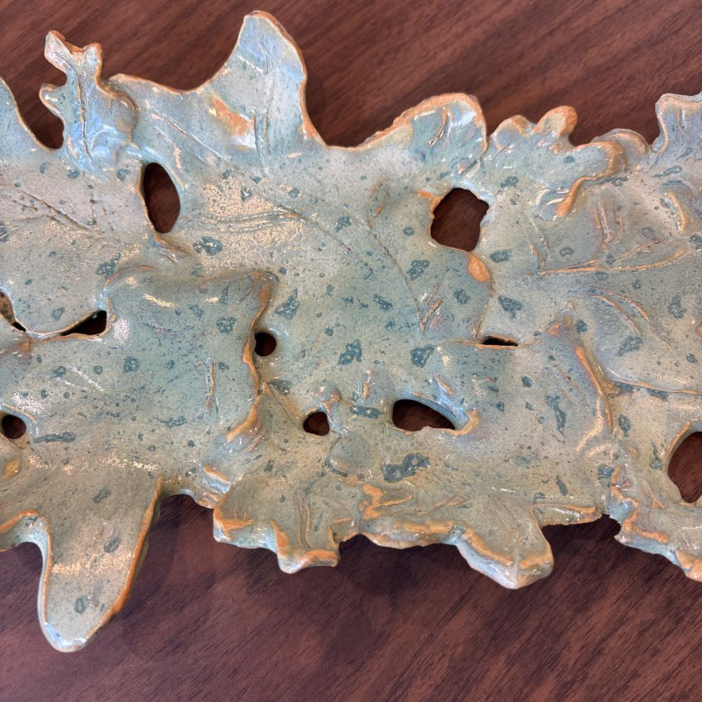 A green ceramic tray of leaves pieced together on a wooden surface and in a store setting.