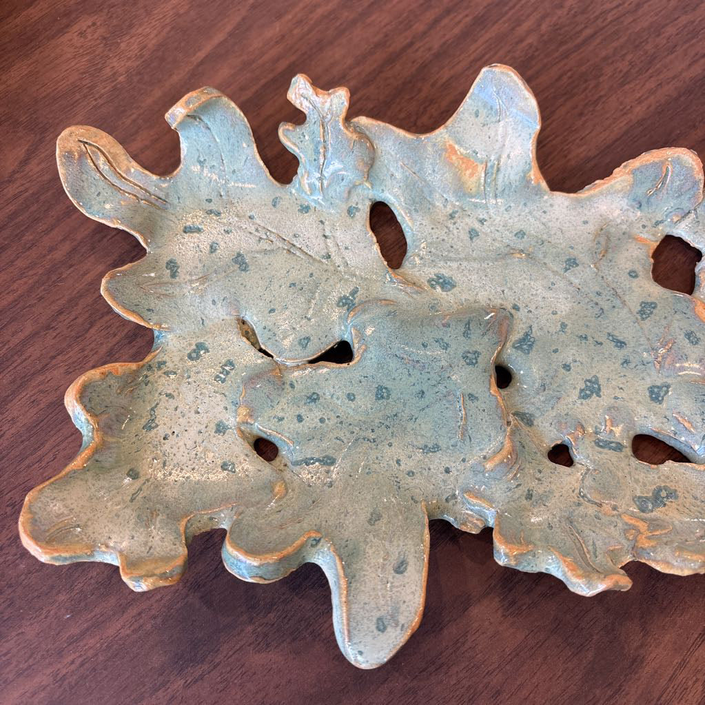 A green ceramic tray of leaves pieced together on a wooden surface and in a store setting.