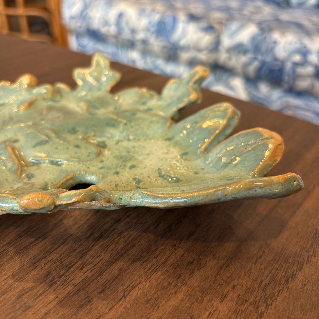 A green ceramic tray of leaves pieced together on a wooden surface and in a store setting.