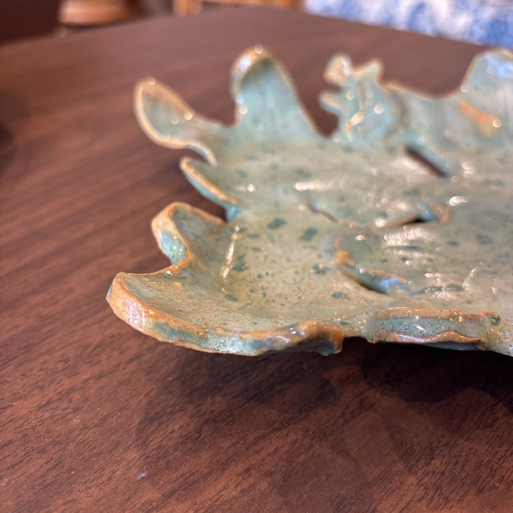 A green ceramic tray of leaves pieced together on a wooden surface and in a store setting.