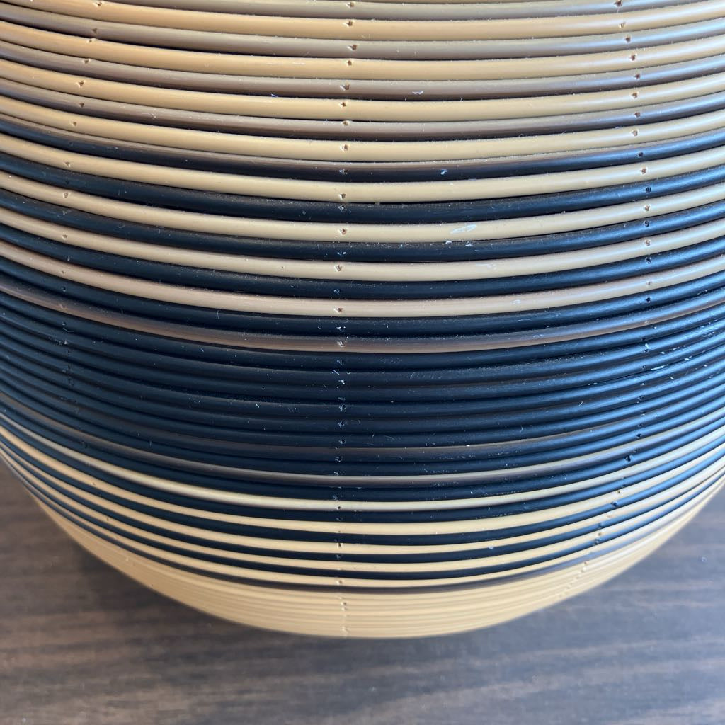 A close-up of a round decorative object with alternating horizontal stripes of dark navy blue and warm beige, resting on a dark wood surface.