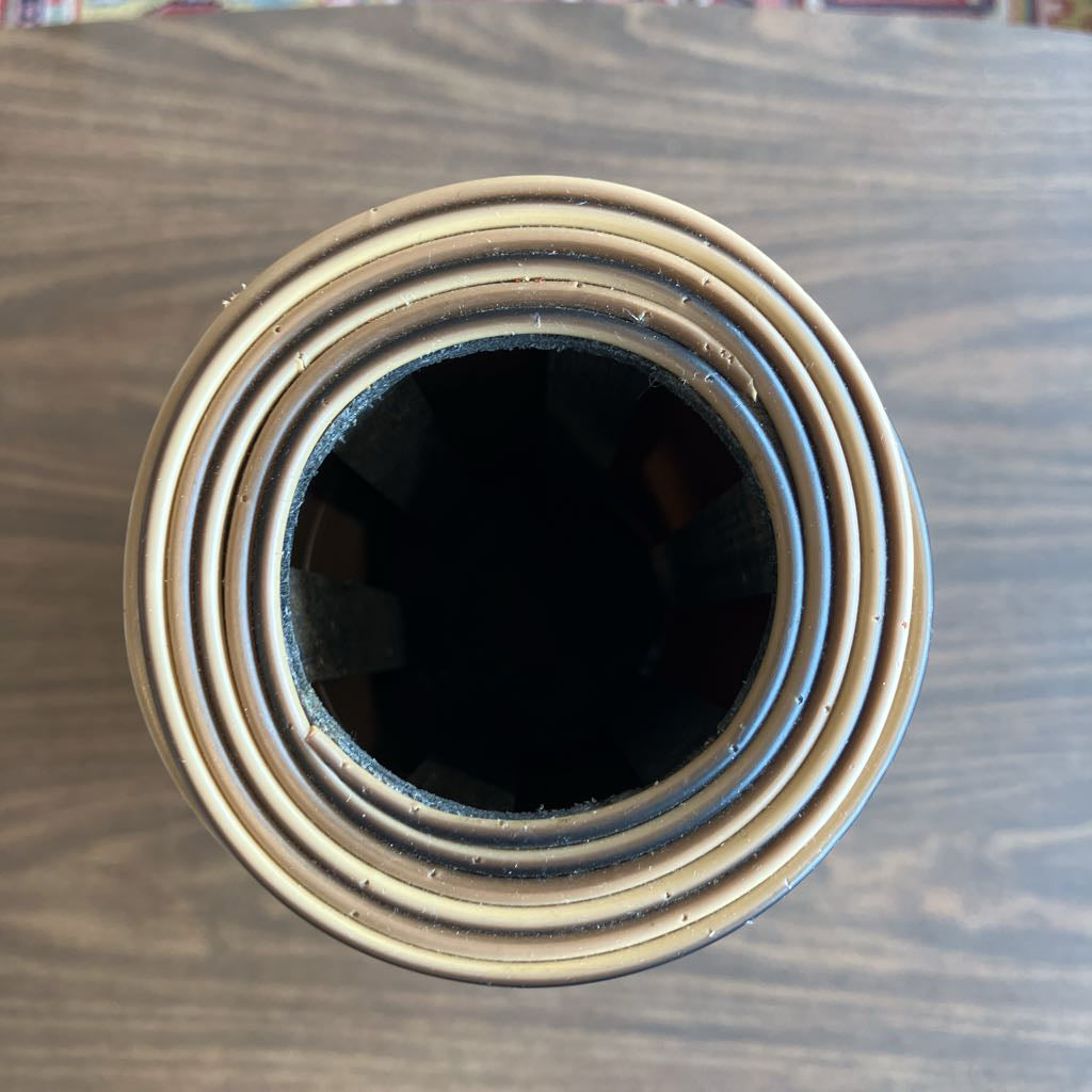 A top-down view of a circular, multi-ring container or candle holder with a dark interior, set on a dark wood-grained surface.