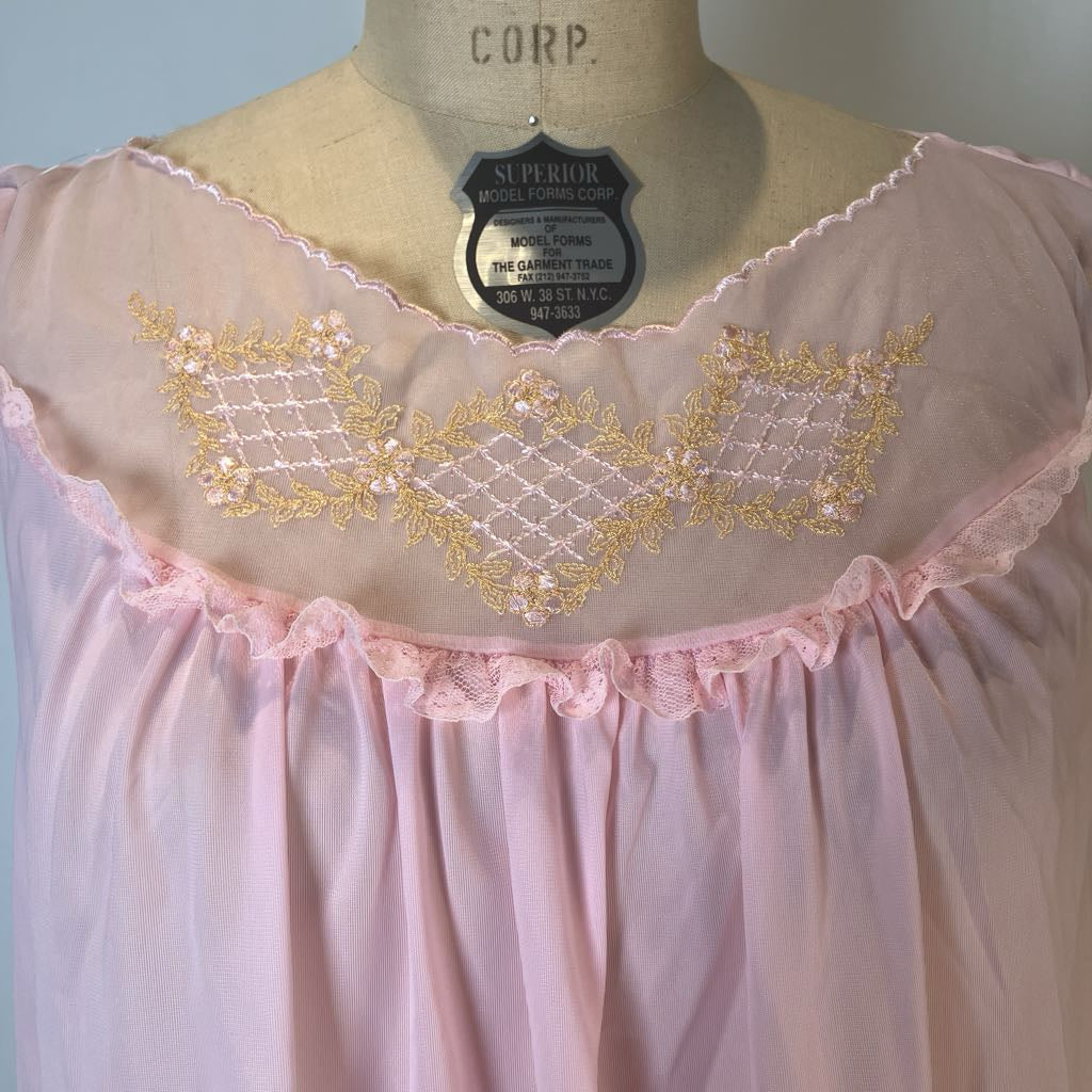 A light pink nightgown with gold embroidered diamond patterns and a ruffled lace neckline, displayed on a beige dress form mannequin.