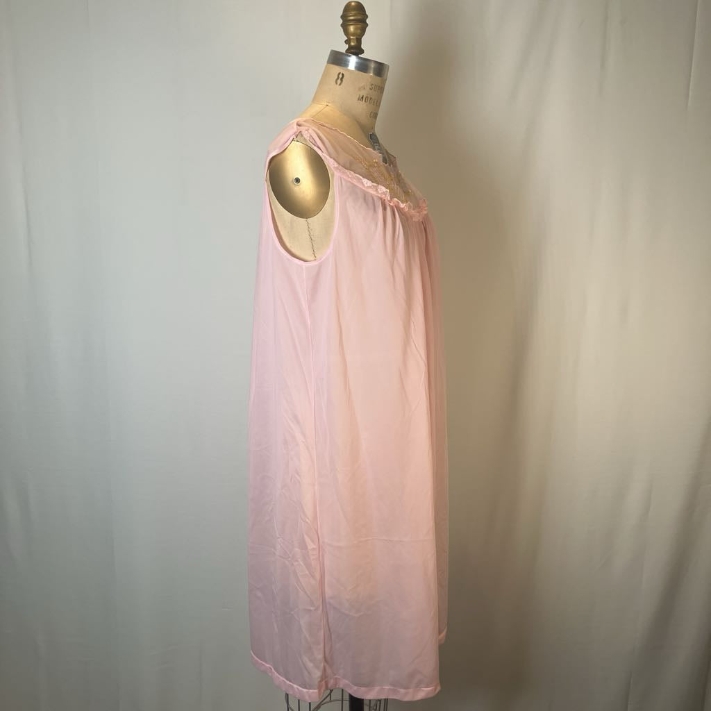 A light pink sleeveless nightgown or chemise displayed on a gold dress form mannequin against a draped off-white fabric backdrop.