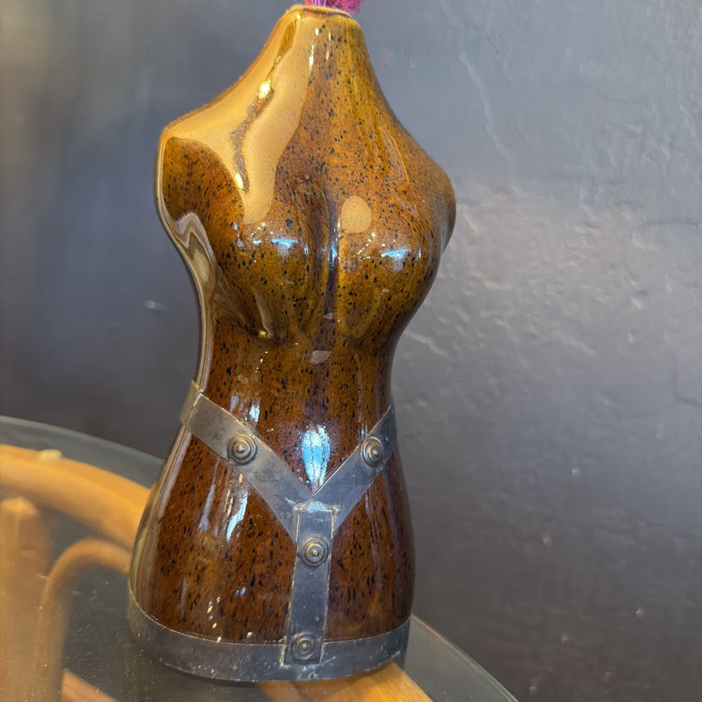 Brown ceramic female torso with metal vase with a few pink flowers coming out