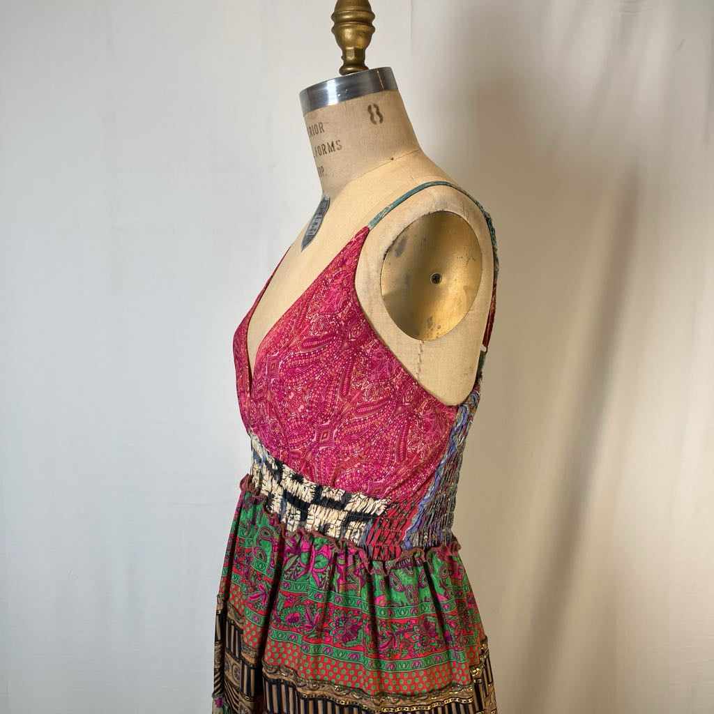 A sleeveless V-neck dress displayed on a vintage wooden dress form mannequin. The dress features a vibrant pink and red patterned bodice with a black and white patterned waistband and a multicolor patterned skirt.