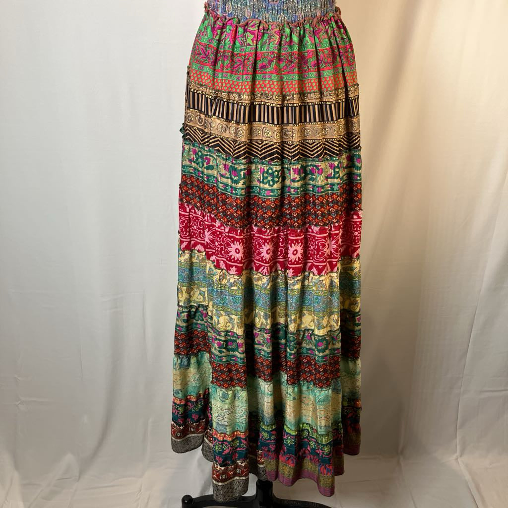 A long bohemian maxi skirt with a vibrant multicolor pattern of red, green, blue, yellow, and brown geometric and tribal motifs, displayed on a black dress form against a white fabric backdrop.