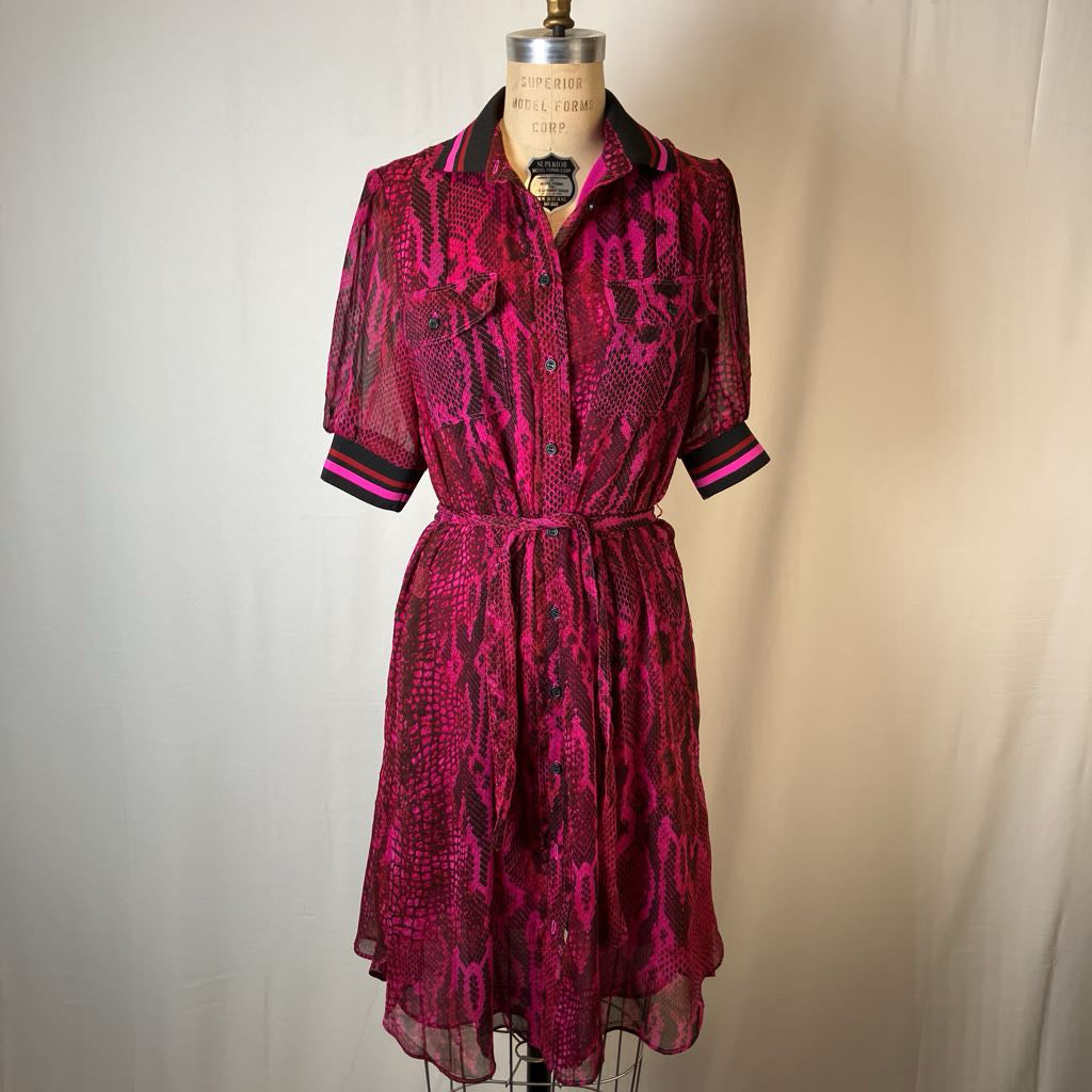 A short-sleeve collared shirt dress with a pink and black snakeskin pattern, displayed on a dress form against a light beige fabric backdrop.