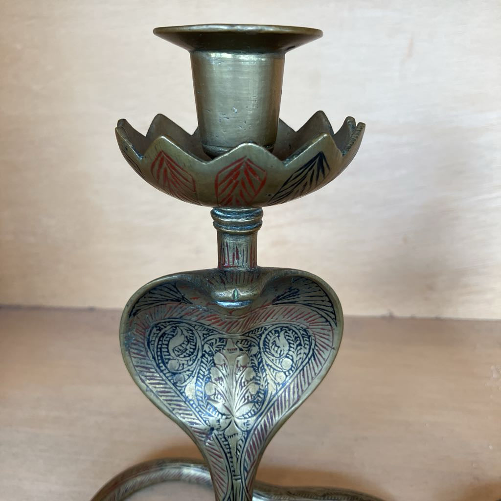 An ornate vintage-style metal candlestick holder with a lotus-shaped cup and a heart-shaped base decorated with engraved floral patterns and red accents, set against a plain beige background.