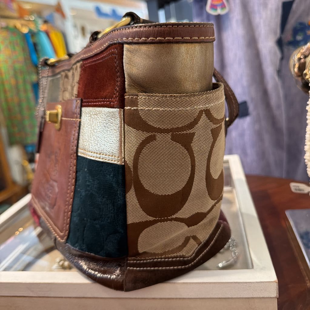 A Coach patchwork shoulder bag with brown leather and signature monogram canvas panels, displayed on a white shelf in a retail setting.