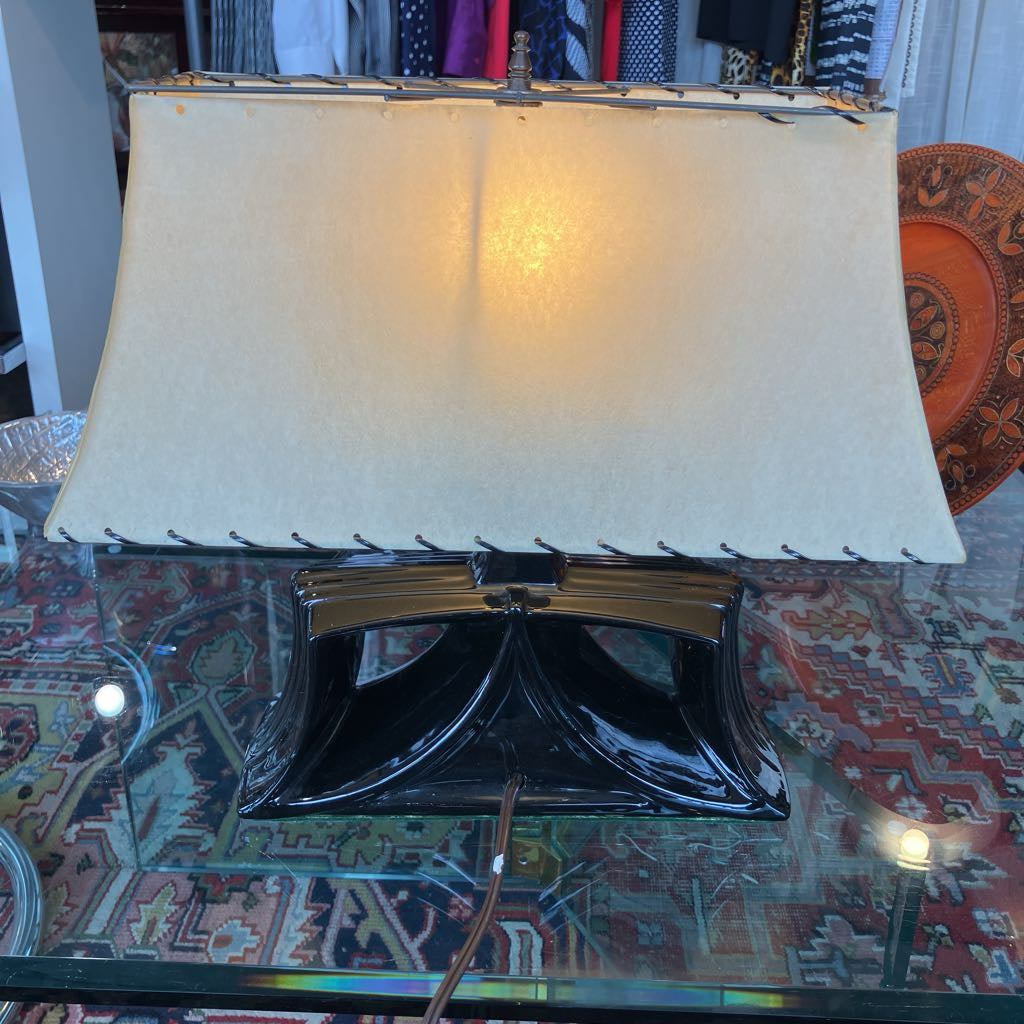 A vintage-style table lamp with a large cream fabric shade and a glossy black sculptural base, shown on a glass table in a home setting.