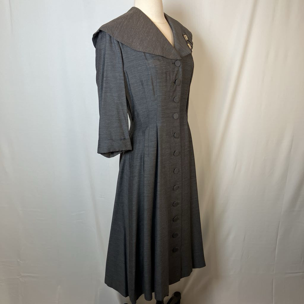 A dark gray textured dress with a wide collar and front button closure, displayed on a mannequin against a white fabric backdrop.