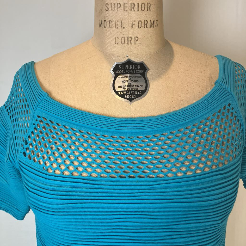 A bright turquoise blue knit top displayed on a beige mannequin torso. The top features a wide scoop neckline with a large open-knit mesh pattern across the chest and short sleeves.