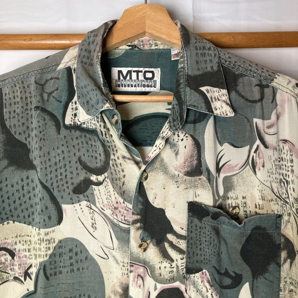 A vintage MTO International patterned short-sleeve button-down shirt hanging on a wooden hanger against a white background.