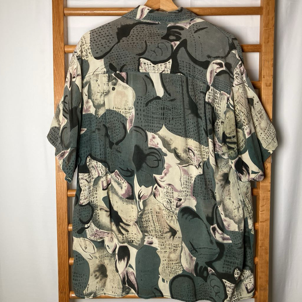 A short-sleeve button-up shirt with an abstract collage print of muted greens and beiges.
