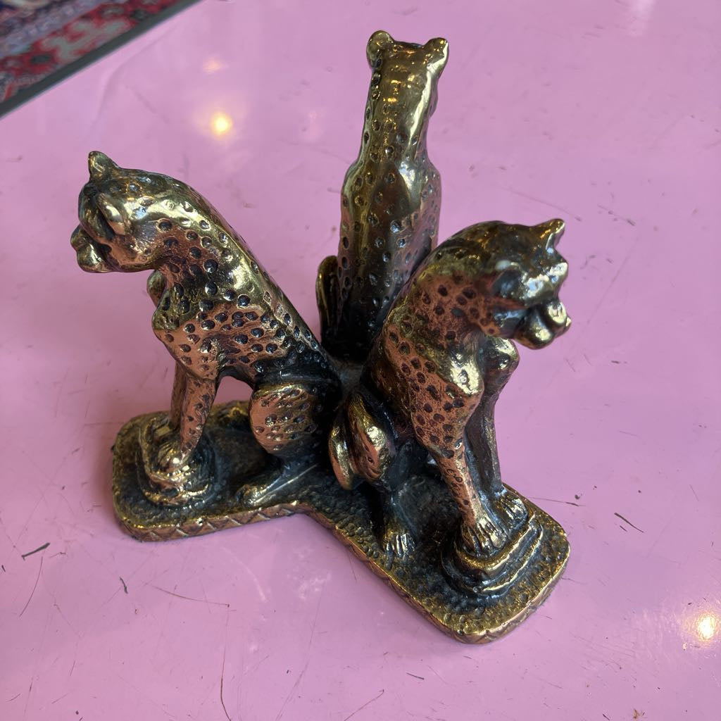 A vintage-style three cat figurine in a bronze finish, displayed on a pink surface.