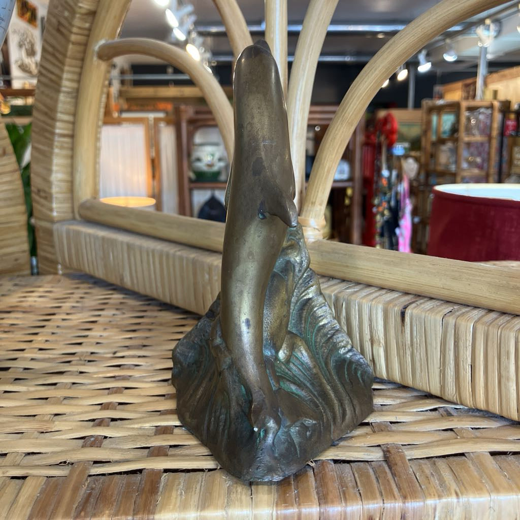 A bronze-finished sculpture of a dolphin rising from stylized waves, displayed on a woven rattan surface inside a shop.