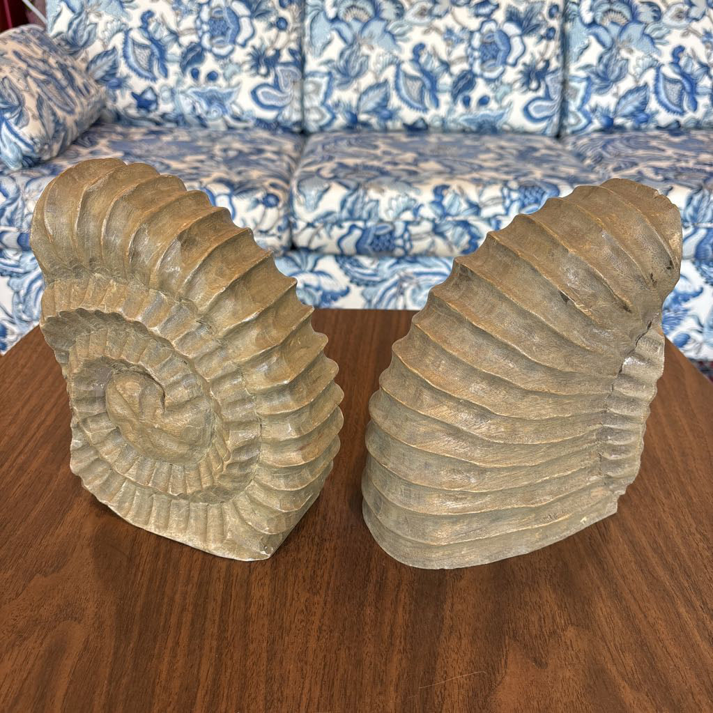 A pair of large faux ammonite bookends displayed on a wooden table in front of a blue and white floral sofa.