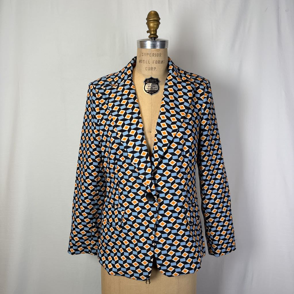 A blazer with a blue and orange geometric pattern on a mannequin against a white wall.