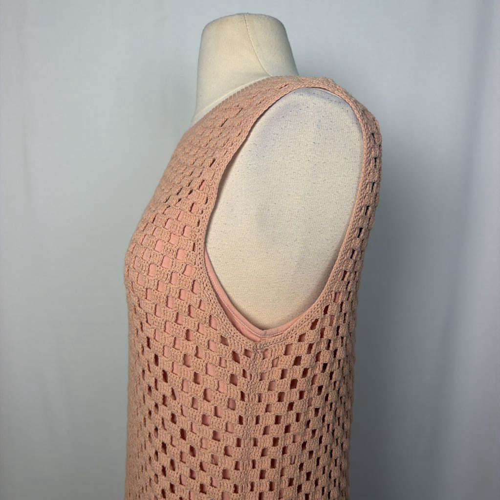 A peach-pink open-knit sleeveless top displayed on a cream mannequin torso against a light gray fabric backdrop.