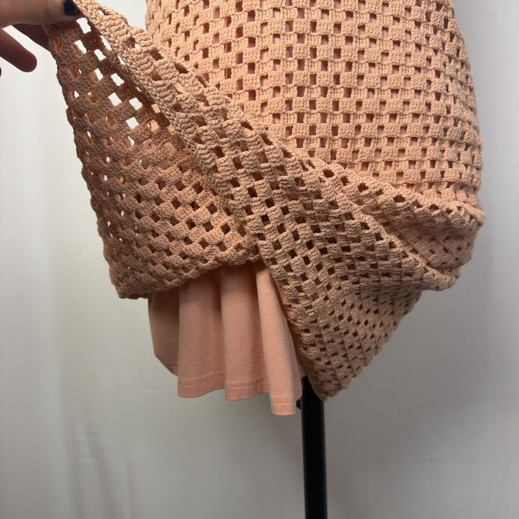 A peach-colored crochet mesh wrap or shawl draped over a peach-colored t-shirt, displayed on a black dress form stand against a white background.