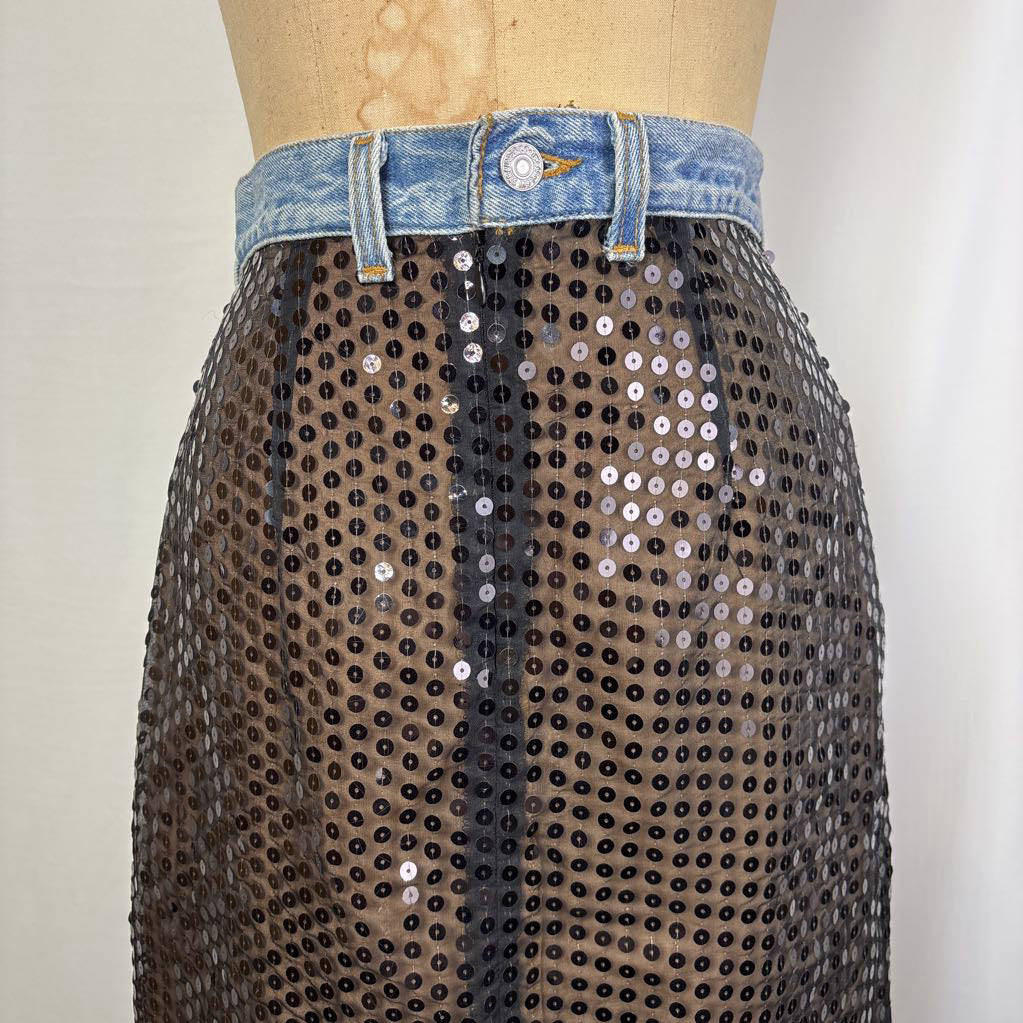 A sheer black sequin skirt displayed on a mannequin torso, styled with a light blue denim waistband at the top.