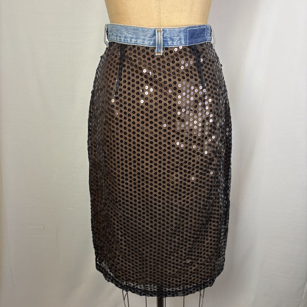 A black sequined mesh pencil skirt displayed on a mannequin torso with a blue denim waistband, set against a plain light gray fabric backdrop.