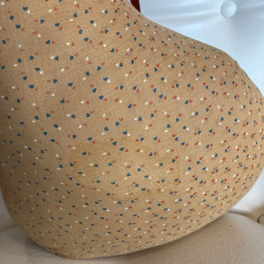 A close-up of a beige fabric cushion or pillow with a small scattered multicolor pattern of tiny hearts and dots in navy, red, and white, resting on a light-colored upholstered surface.