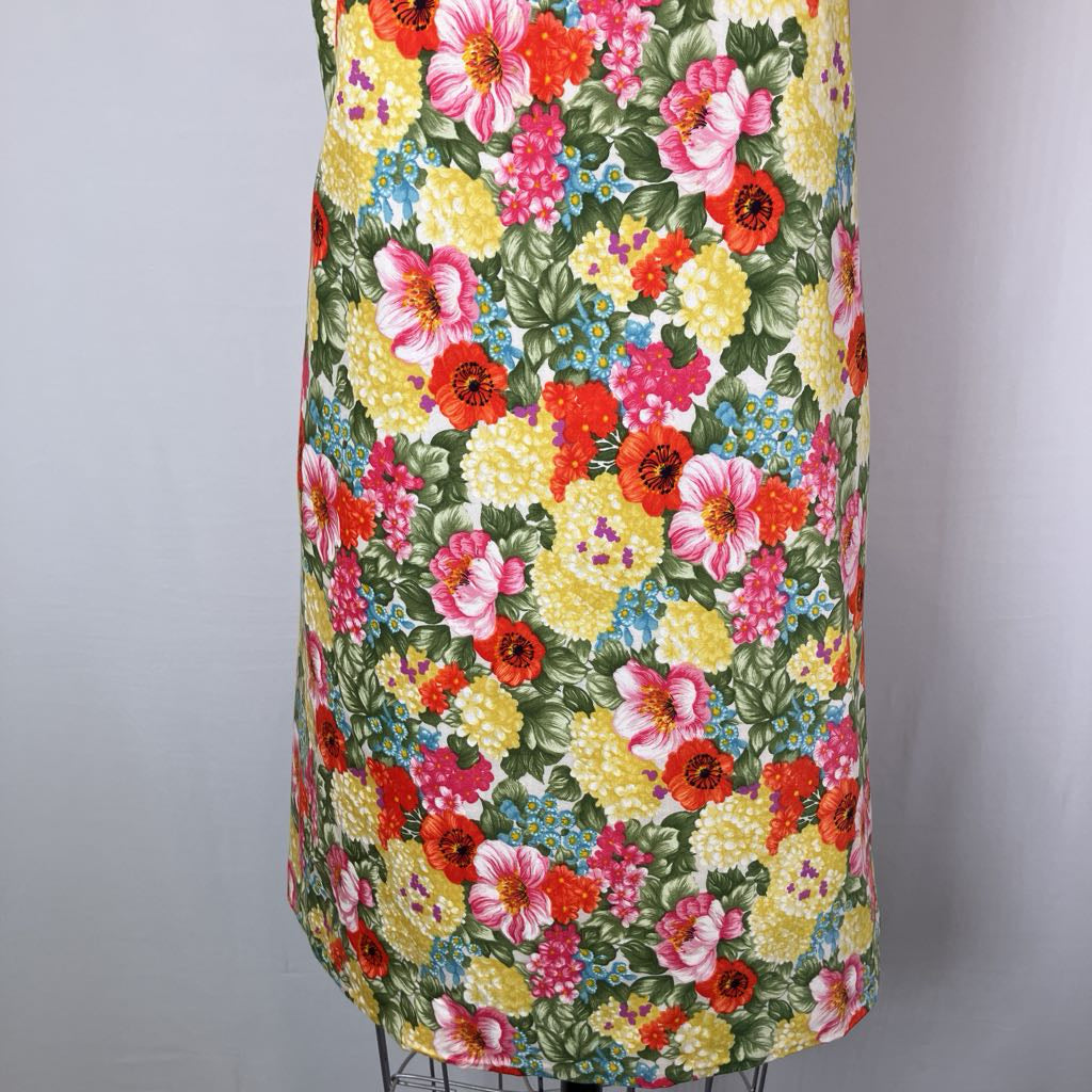 A sleeveless dress with a dense, colorful floral print featuring pink, red, yellow, and blue flowers on a green background, displayed on a mannequin against a light gray backdrop.