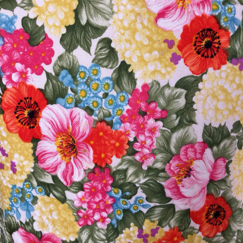 A close-up of a colorful floral fabric print featuring pink, red, yellow, and blue flowers with green leaves on a light background.