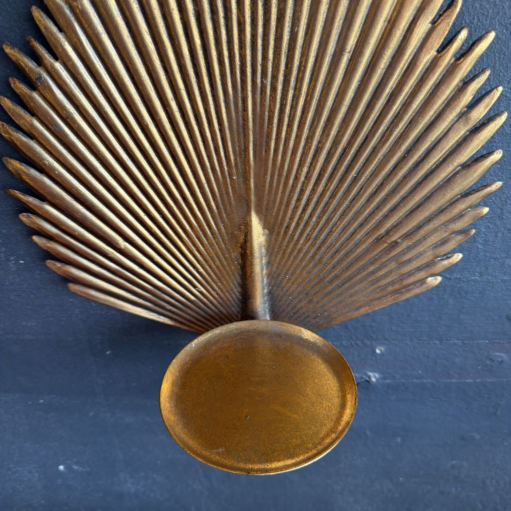 A vintage-style metallic wall sconce featuring a fan or palm leaf design with a circular base, finished in a warm gold/brass tone against a dark textured background.