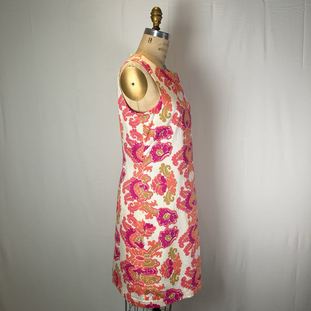 A sleeveless shift dress with a vibrant floral and paisley print in pink, orange, and green on an off-white background, displayed on a vintage dress form mannequin.