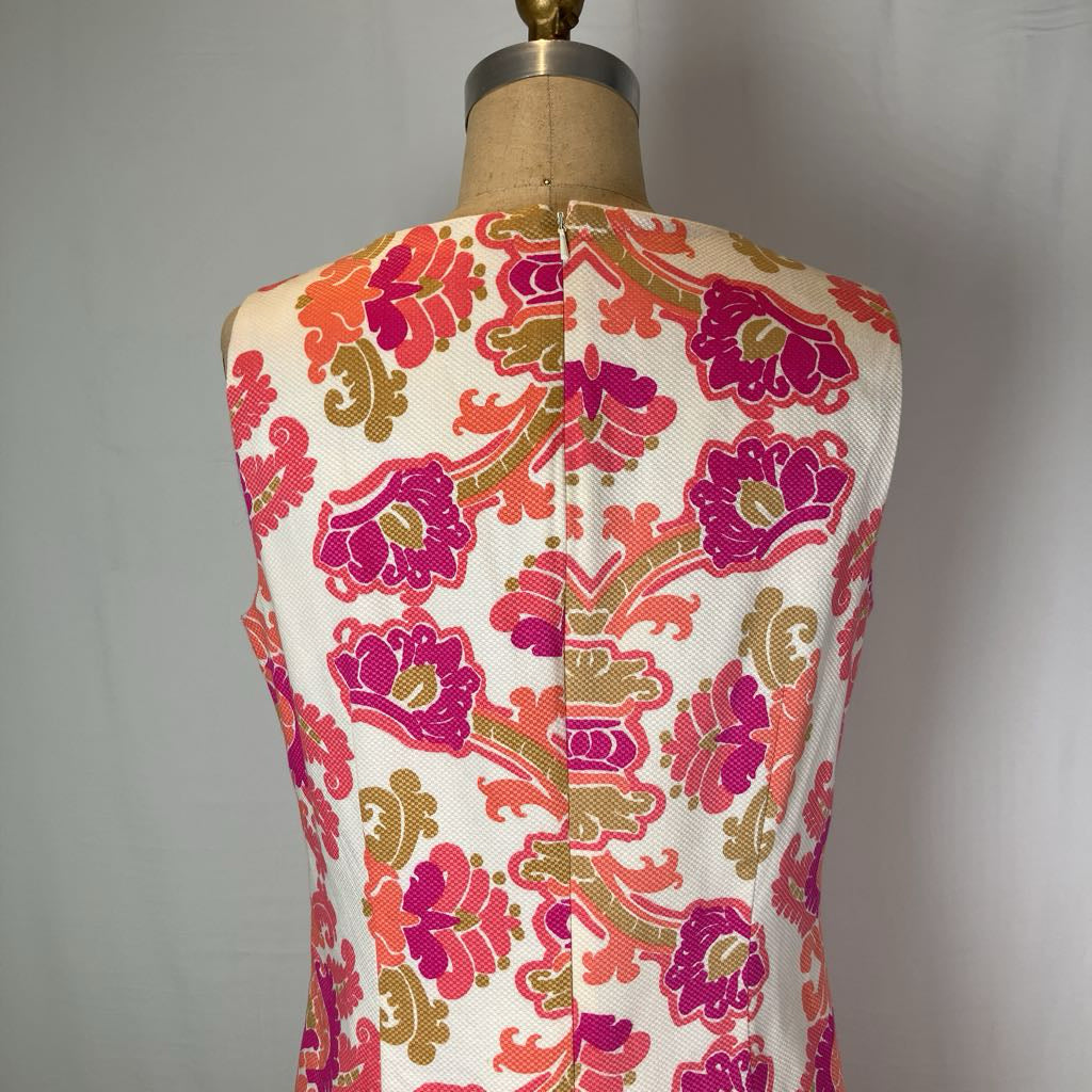 A sleeveless vest or top displayed on a dress form, showing the back view with a colorful floral and scroll pattern on an off-white base. The print features bright pink, orange, and olive green motifs.