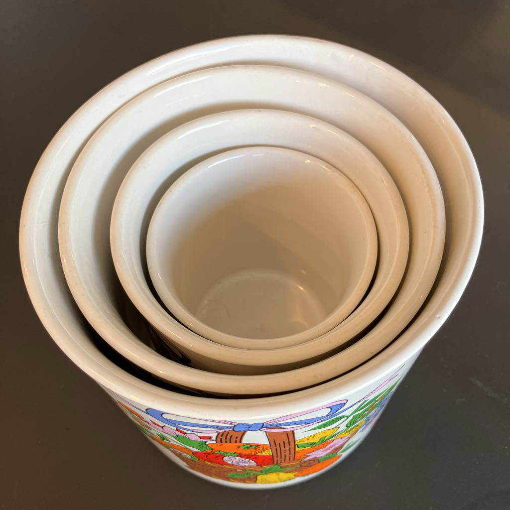 A set of nested white ceramic bowls with a colorful illustrated pattern on the outer rim, photographed from above on a dark gray surface.
