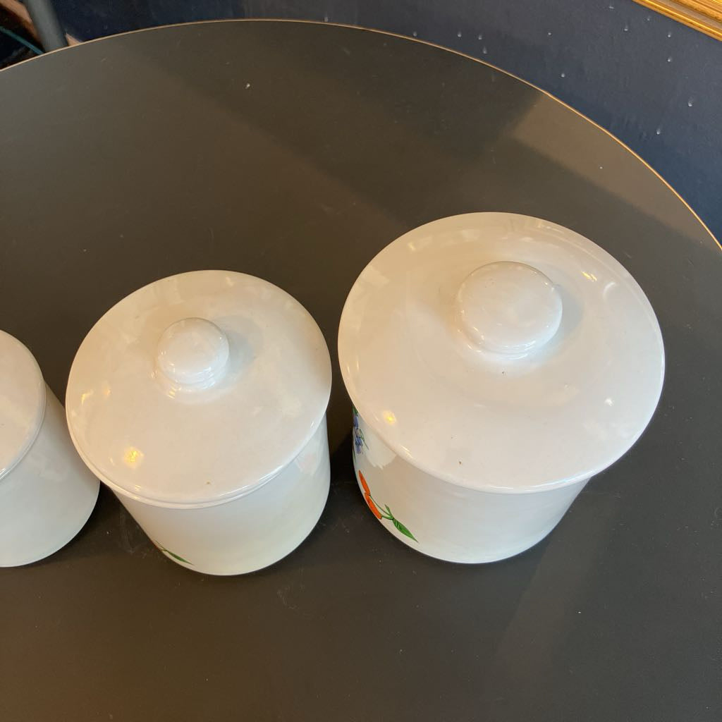 Three white ceramic lidded containers with ribbed screw-top lids arranged on a dark reflective surface.