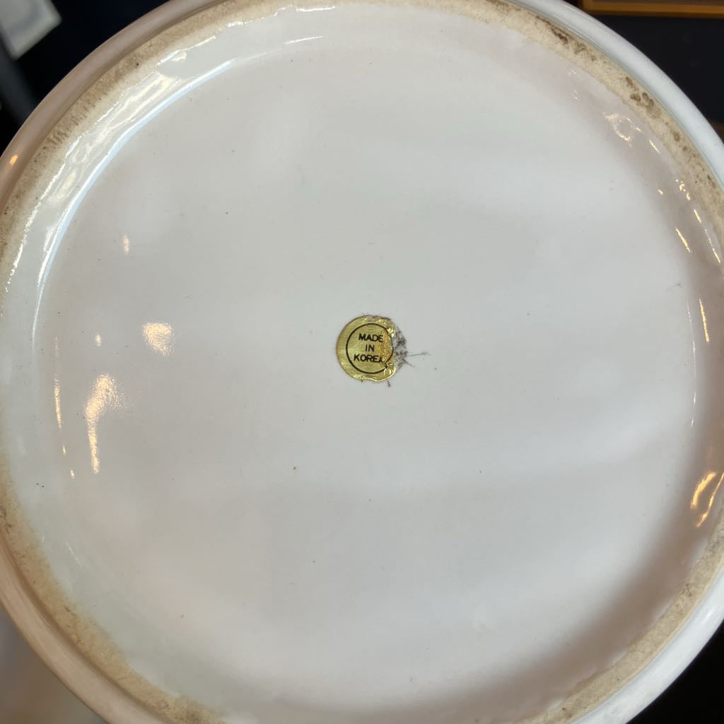 Close-up bottom view of a white ceramic plate or bowl showing a small round gold brand seal in the center and a slightly worn beige rim.